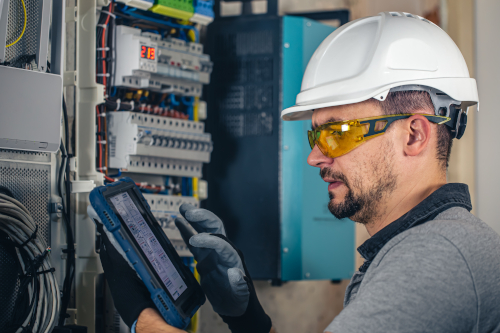 Man, an electrical technician working in a switchboard with fuses. Man, an electrical technician working in a switchboard with fuses. Installation and connection of electrical equipment. Professional uses a tablet.