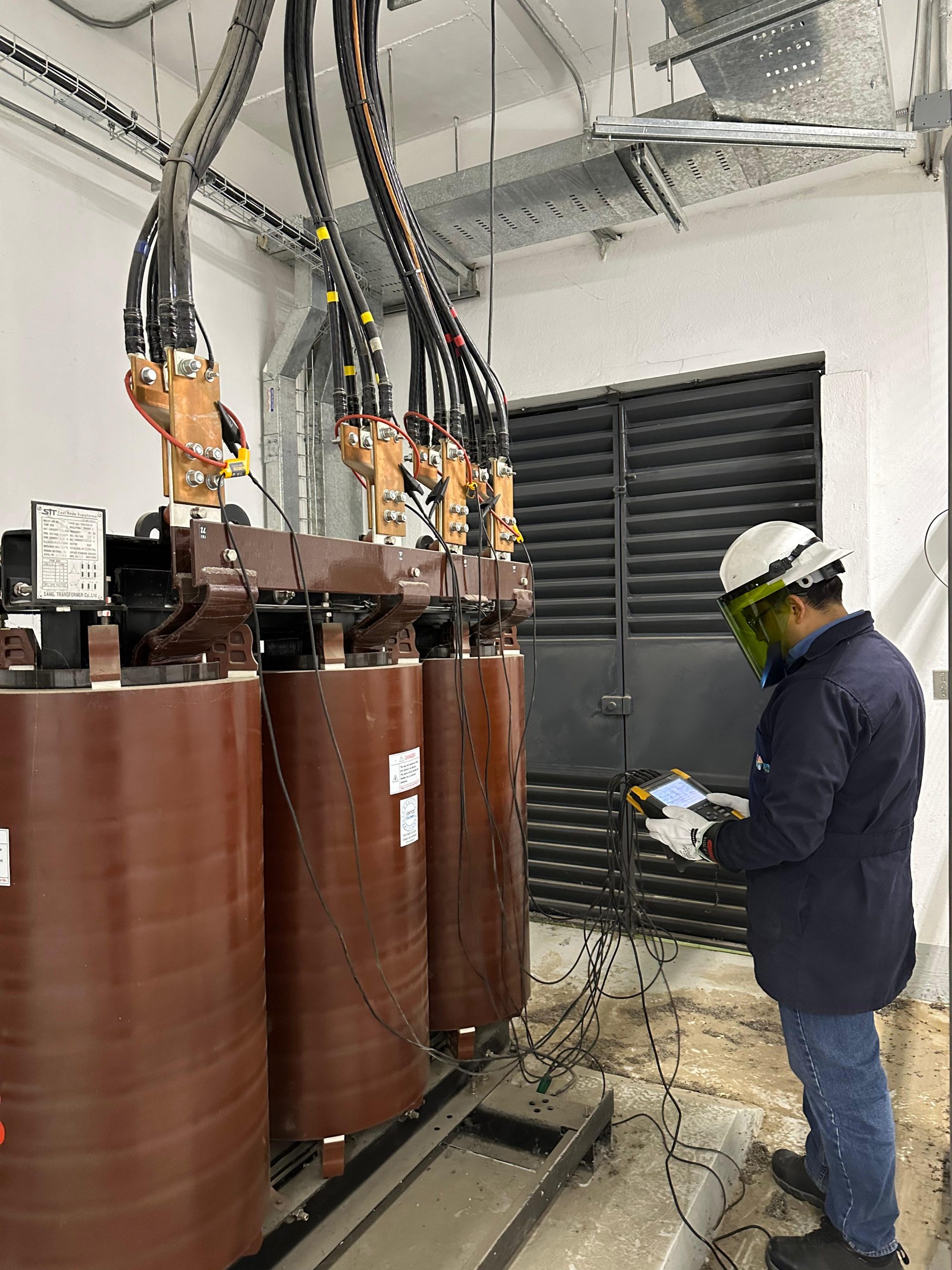 Técnico de Adenyr realizando mediciones eléctricas con un analizador junto a un transformador industrial
